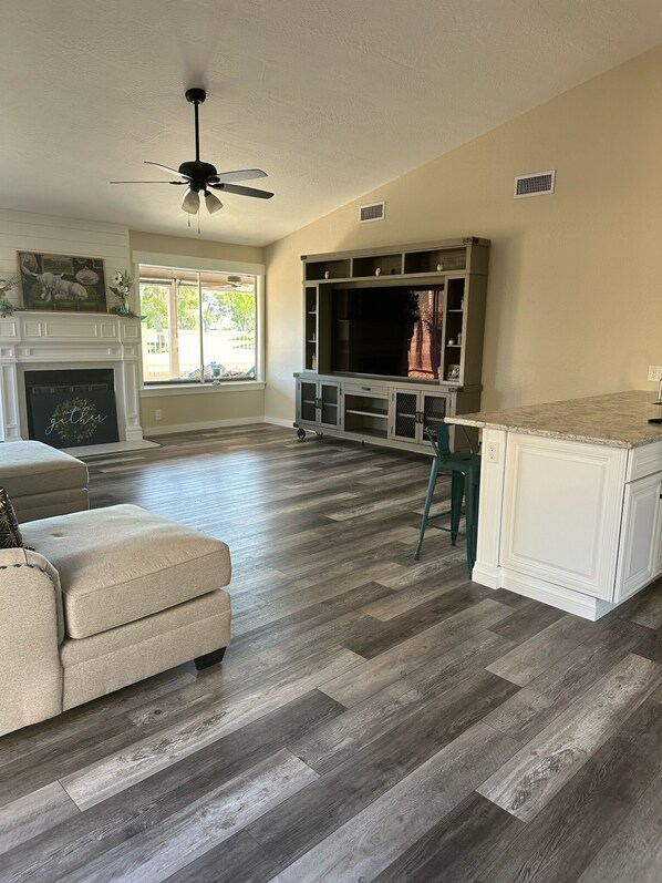 A spacious living room with a fireplace, a large TV, and a ceiling fan. - 3 bedroom house in Mesa w/heated pool and golf course views (Mesa)