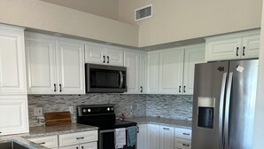 A modern kitchen with white cabinets, a stainless steel refrigerator, a microwave, and an oven. - Remodeled 3 bedroom house in Mesa w/heated pool and golf course views (Mesa)