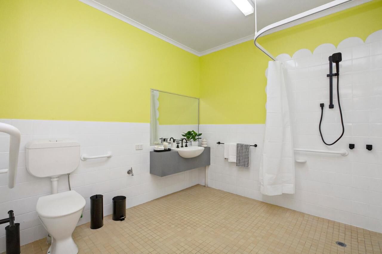 Un baño con inodoro blanco, lavamanos con espejo, ducha con cortina y suelo de baldosas.