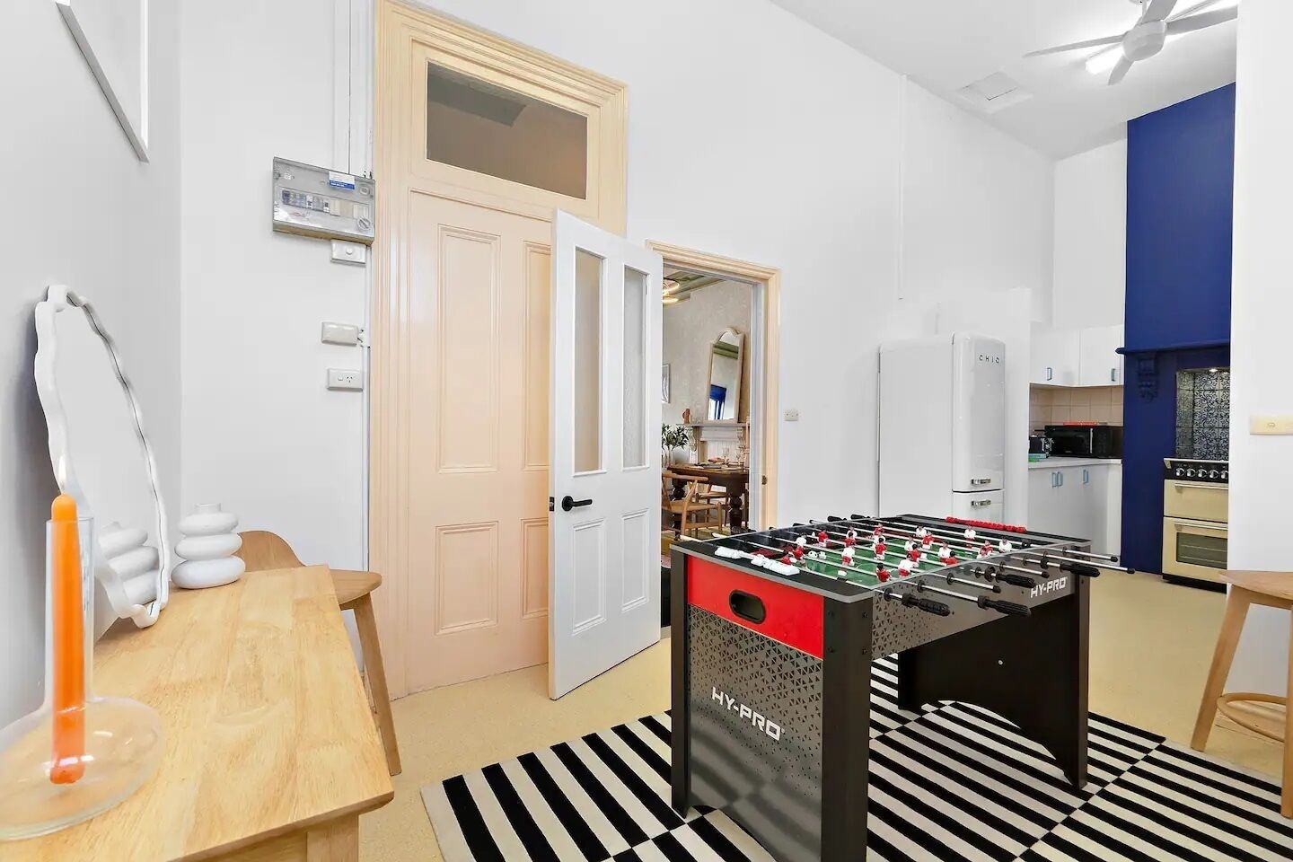 A modern kitchen with a foosball table, a dining area with a wooden table and chairs, and a kitchen counter with appliances.