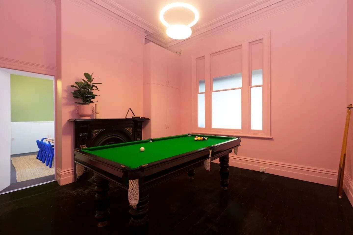 A room with a pool table, a potted plant, and a window with blinds.