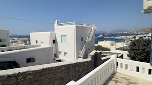 A coastal building with a stone wall and white railings, a staircase, and a view of the sea and distant boats. - Selini KHORA (Mikonos)