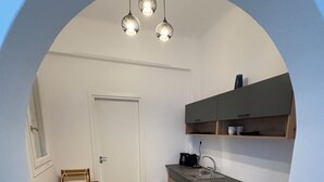 A compact kitchen with a white door, wooden cabinets, a countertop, and a speckled floor. - Selini KHORA (Mikonos)