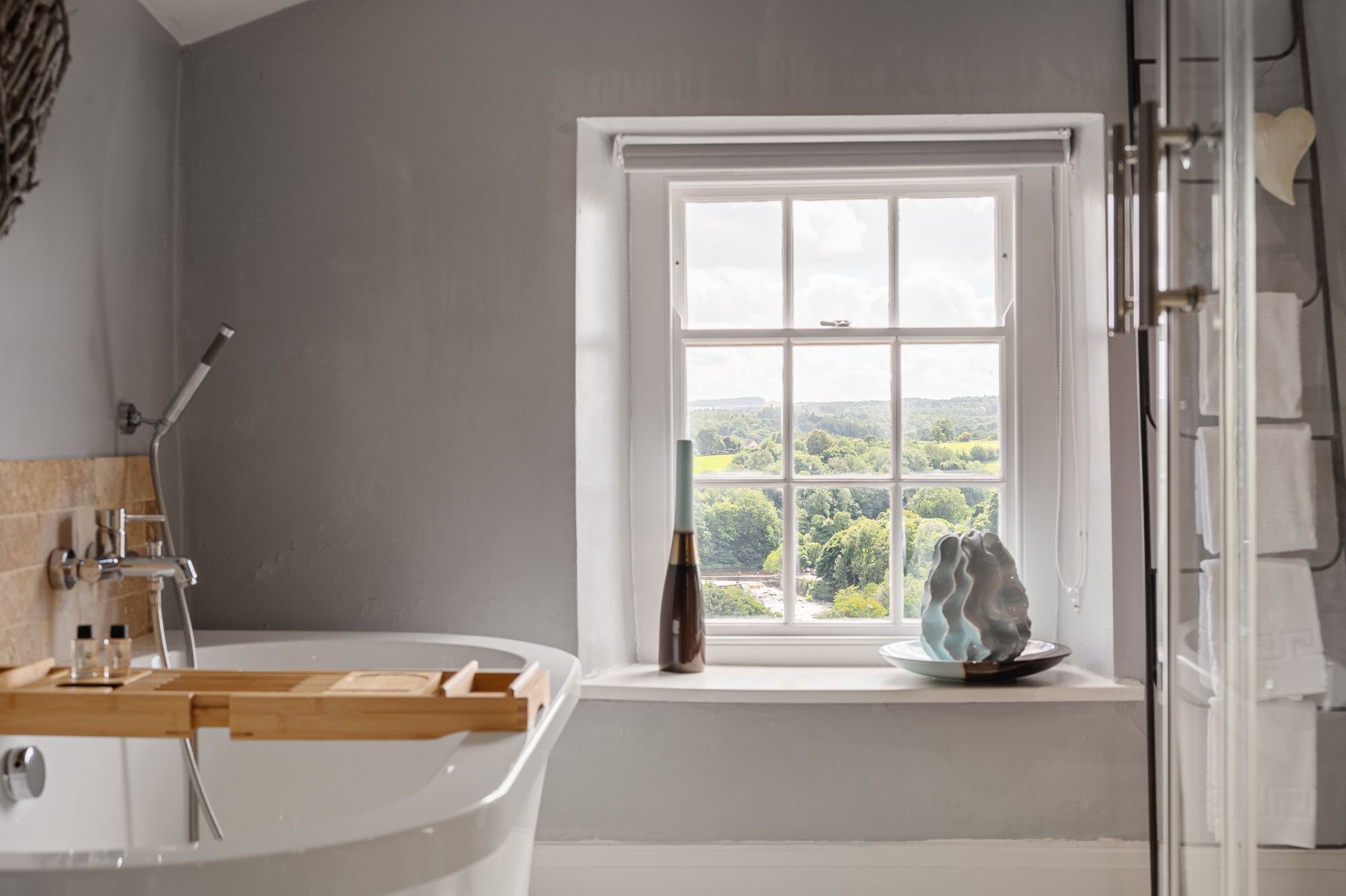 A bathroom with a bathtub, a window with a view of greenery, and a towel rack.