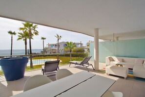 A balcony with a white table and chairs, a blue planter, and a view of the ocean and palm trees. - Happy Travel South Beach 1-1b (Benalmádena)