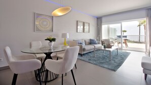 A modern living room with a glass dining table, white sofas, and a blue rug.
