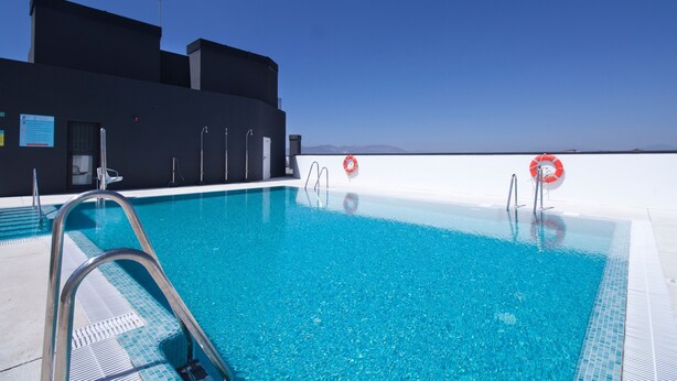 Ein klares, blaues Schwimmbecken mit einer Metallleiter, Rettungsringen und einem modernen Gebäude im Hintergrund.