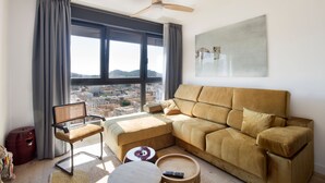 Ein modernes Wohnzimmer mit großem Fenster, einer Couch, einem Sessel und einem kleinen Tisch.