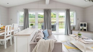 Een ruime kamer met een grote schuifpui naar een terras, een bank, een eettafel met stoelen, en een klein kastje.