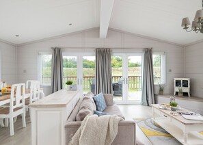 A spacious room with a large sliding glass door leading to an outdoor deck, a sofa, a dining table with chairs, and a small cabinet.