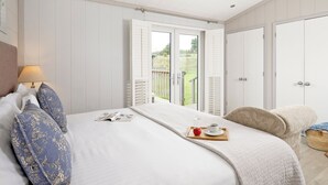 Een slaapkamer met een bed, een nachtkastje met een lamp, een raam met uitzicht op het landschap en een deur.