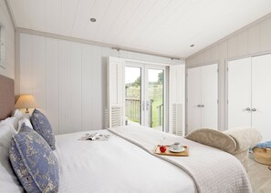 A bedroom with a bed, a bedside table with a lamp, a window with a view of the outdoors, and a door.