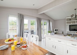 Une cuisine avec une table à manger préparée pour le petit-déjeuner, un téléviseur et une vue sur l’extérieur.