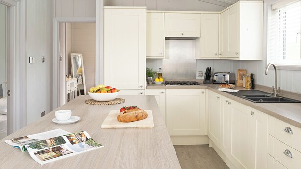 Een moderne keuken met witte kasten, een centraal kookeiland met een schaal fruit en brood, een fornuis en een spoelbak.