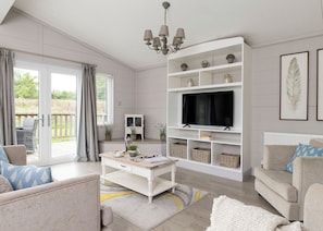 Un salon avec un téléviseur, des étagères blanches, un canapé, une table basse et une vue sur l’extérieur, visible à travers une porte vitrée.