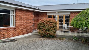 A two-story brick house with a covered porch, a small garden, and a metal fence. - Home Sweet Home (Timaru)