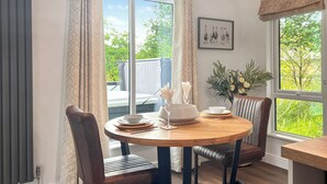 Een eethoek met een ronde tafel, stoelen, een vaas met bloemen en een raam met uitzicht op groen.