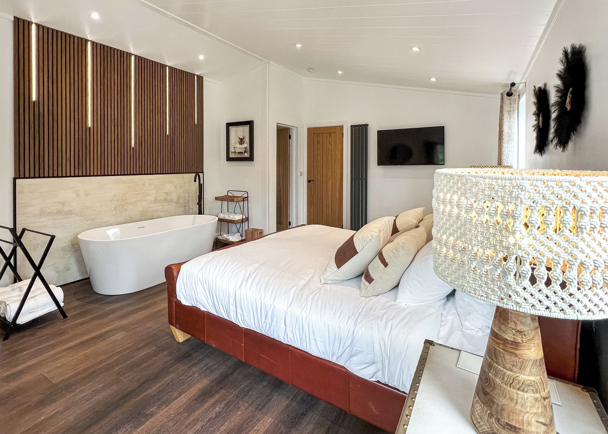 Une chambre à coucher avec un grand lit, une baignoire, un lambris en bois, une télévision et une lampe décorative.