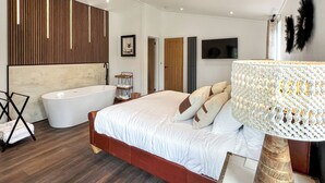 Een slaapkamer met een groot bed, een badkuip, houten lambrisering, een televisie en een decoratieve lamp.