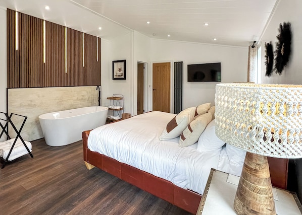 Un dormitorio con una cama grande, una bañera, paneles de madera, un televisor y una lámpara decorativa.