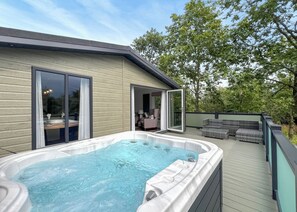 A hot tub on a wooden deck with a glass door leading to an interior room.