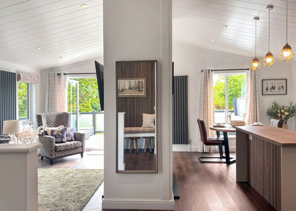 A modern living room with a sofa, a dining area with a table and chairs, and a kitchen area with a counter and pendant lights.