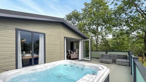 Een hottub op een houten terras, met een glazen deur naar een binnenruimte.