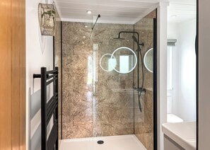 Un bagno moderno con box doccia in vetro, pareti in marmo e una mensola in metallo nero.