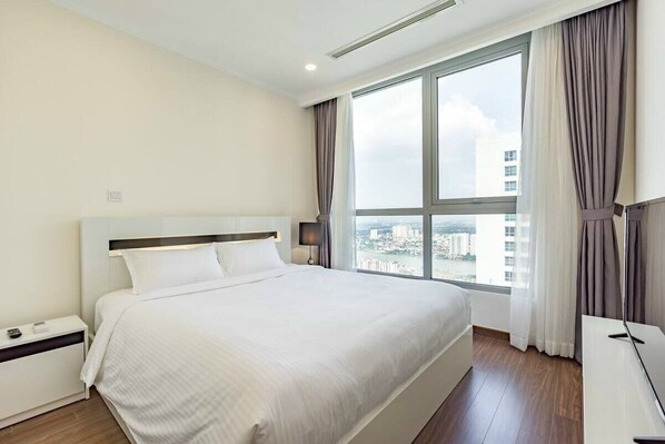 A hotel room with a large bed, a nightstand, a desk, and a window with curtains.