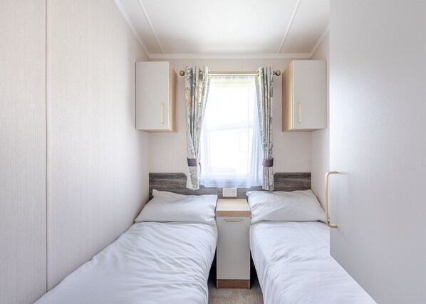 A compact bedroom with two single beds, a small window with curtains, and a wooden headboard. - Coldstream Retreat - 3 Bedroom (Pet Friendly) (Coldstream)