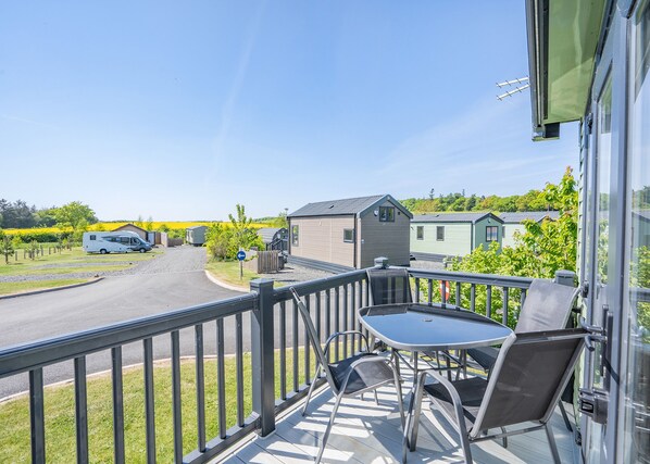 A balcony with a table and chairs, a view of a road, and a row of small buildings. - Coldstream Retreat - 3 Bedroom (Pet Friendly) (Coldstream)
