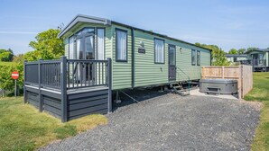 A green mobile home with a fenced porch, a hot tub, and a gravel driveway. - Coldstream Retreat - 3 Bedroom (Pet Friendly) (Coldstream)