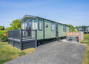 A green mobile home with a fenced porch, a hot tub, and a gravel driveway. - Coldstream Retreat - 3 Bedroom (Pet Friendly) (Coldstream)