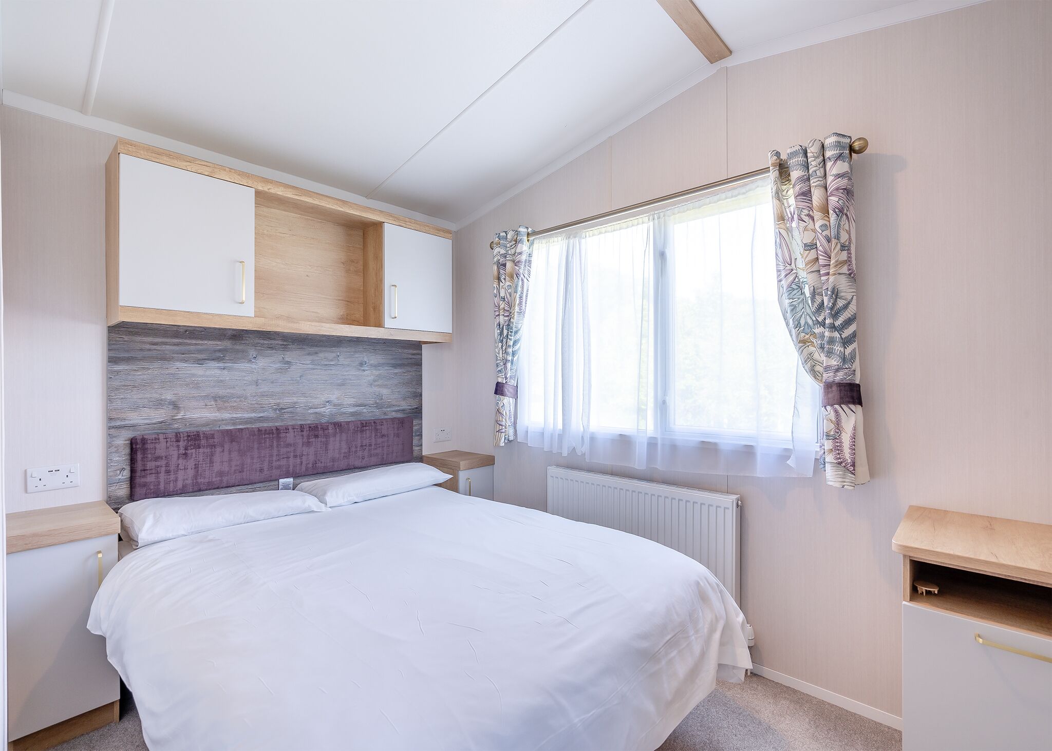 Ein Schlafzimmer mit einem Bett, einem Holz-Kopfteil, einem Fenster mit Vorhängen und eingebauten Schränken.