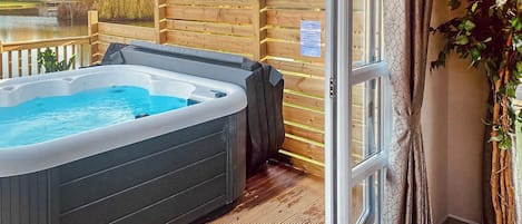 Un bain à remous sur une terrasse en bois, avec vue sur un lac et des arbres.