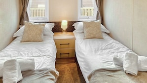A twin room with two beds, a nightstand with a lamp, and a window with curtains.
