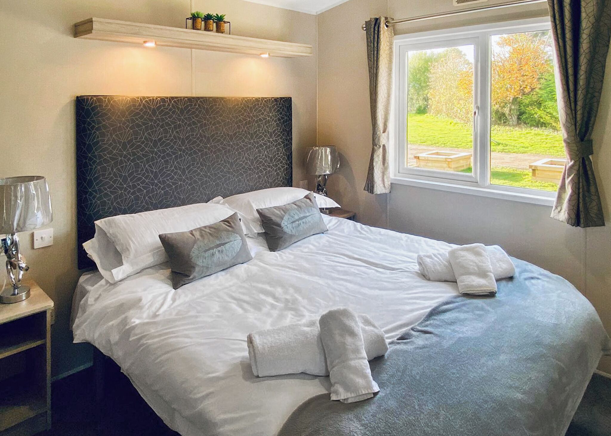 A neatly made bed with pillows and towels, a bedside lamp, and a window with curtains.