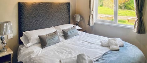 Ein ordentlich bezogenes Bett mit Kissen und Handtüchern, eine Nachttischlampe und ein Fenster mit Vorhängen.