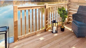 A wooden deck with a railing, a potted plant, a lantern, and a grill area.