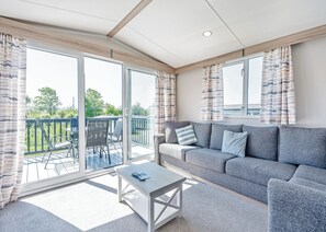 A modern living room with a grey sofa, a small table, and a sliding glass door leading to an outdoor deck. - Tweed Retreat - 2 Bedroom (Pet Friendly) (Coldstream)