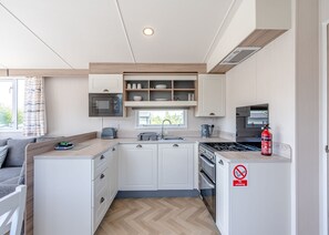A compact kitchen with white cabinetry, a built-in microwave, a stove, and a window above the sink.