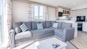 A modern living room with a grey sofa, a coffee table, and a kitchen area in the background. - Tweed Retreat - 2 Bedroom (Pet Friendly) (Coldstream)
