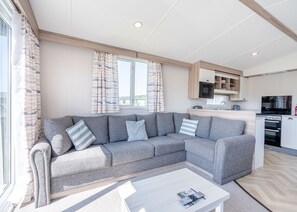 A modern living room with a grey sofa, a coffee table, and a kitchen area in the background. - Tweed Retreat - 2 Bedroom (Pet Friendly) (Coldstream)