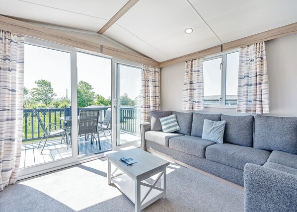 A modern living room with a grey sofa, a small table, and a sliding glass door leading to an outdoor deck.