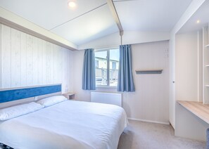 A bedroom with a bed, a window with curtains, a radiator, and a wooden shelf. - Tweed Retreat - 2 Bedroom (Pet Friendly) (Coldstream)