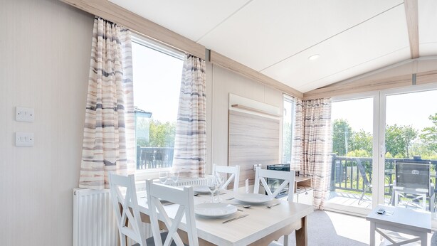 A modern dining area with a table set for two, white chairs, and a view of the outdoors.