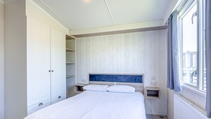 A bedroom with a bed, white wardrobe, wooden panel wall, and a window with curtains.