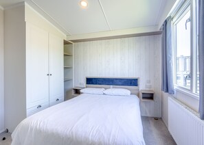 A bedroom with a bed, white wardrobe, wooden panel wall, and a window with curtains. - Tweed Retreat - 2 Bedroom (Pet Friendly) (Coldstream)