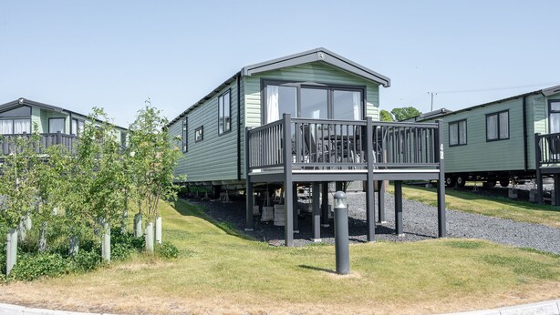 A row of green mobile homes with a central unit featuring a balcony. - Tweed Retreat - 2 Bedroom (Pet Friendly) (Coldstream)