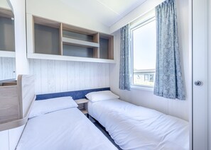 A room with two beds, a window with curtains, and built-in shelves.
